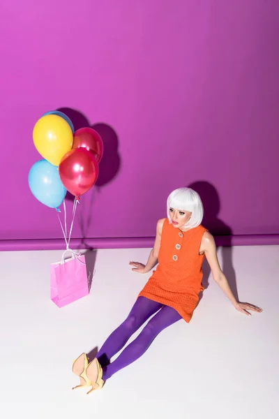 Gorgeous girl in white wig with air balloons sitting on purple background — Stock Photo