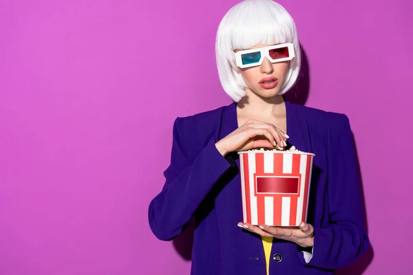 Gorgeous young woman in 3d glasses eating popcorn on purple background — Stock Photo