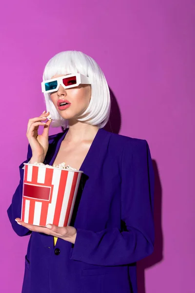 Elegante giovane donna in occhiali 3d mangiare popcorn su sfondo viola — Foto stock