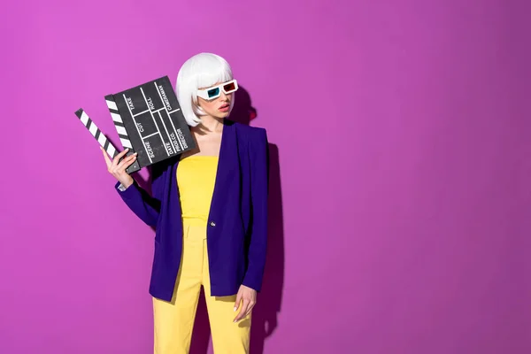 Elegant woman in 3d glasses holding clapperboard and looking away on purple background — Stock Photo