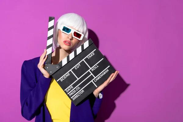 Girl in white wig and 3d glasses holding clapperboard on purple background — Stock Photo
