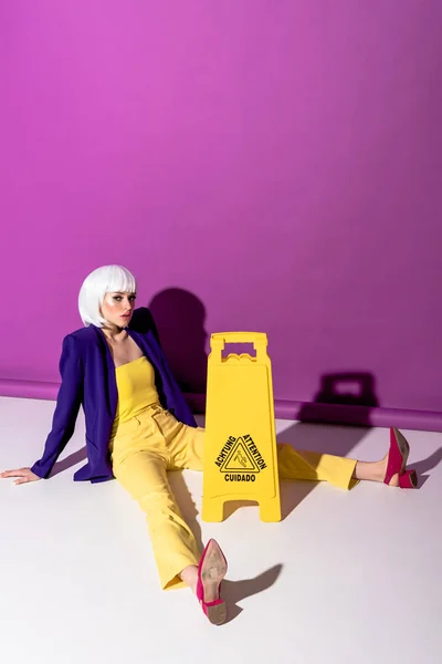 Girl in red shoes sitting near wet floor sign on purple background — Stock Photo