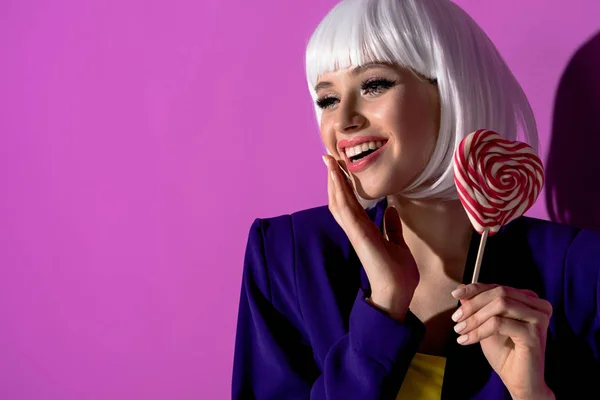 Laughing girl in white wig holding lollipop on purple background — Stock Photo