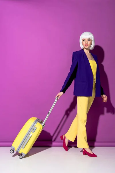 Повнометражний вид на стомлену жінку в перуці з жовтою валізою на фіолетовому фоні — стокове фото