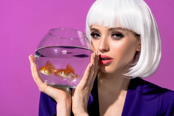 Charmante junge Frau mit weißer Perücke hält Aquarium mit Goldfischen isoliert auf lila — Stockfoto