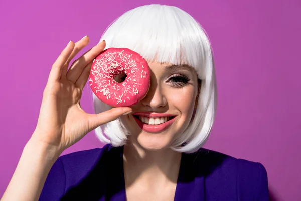Sonriente hermosa chica sosteniendo rosado donut en púrpura fondo - foto de stock