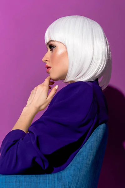 Side view of beautiful woman in white wig sitting in armchair on purple background — Stock Photo