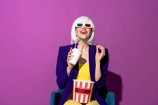 Laughing girl in 3d glasses eating popcorn and drinking soda on purple background — Stock Photo