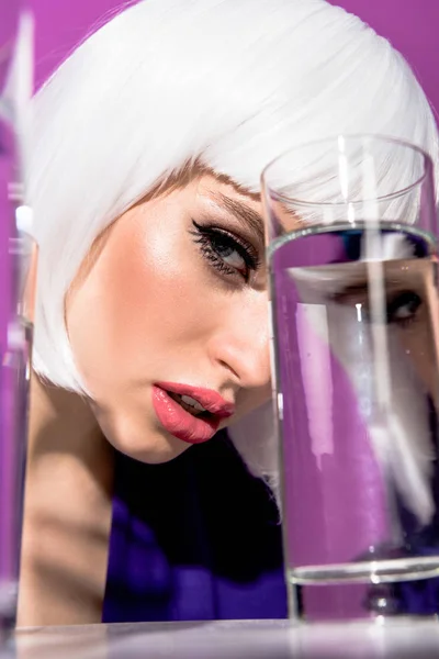 Preciosa mujer en peluca blanca con vaso de agua sobre fondo púrpura - foto de stock