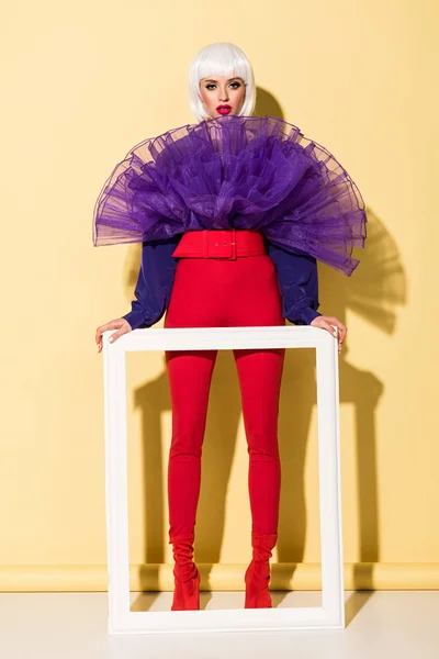 Full length view of woman in white wig holding frame on yellow background — Stock Photo