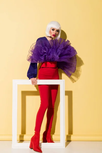 Full length view of fashionable woman in wig with frame on yellow background — Stock Photo