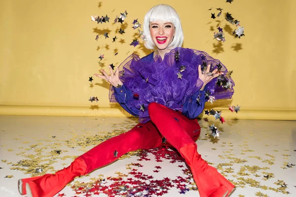 Laughing woman in red pants throwing out sparkle confetti on yellow background — Stock Photo