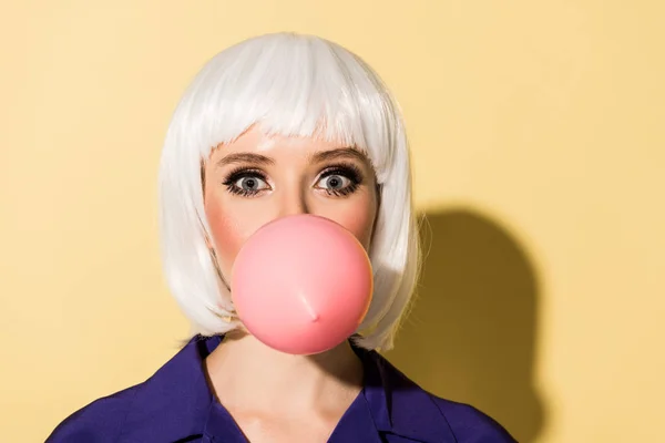 Amazed girl in white wig chewing bubble gum on yellow background — Stock Photo