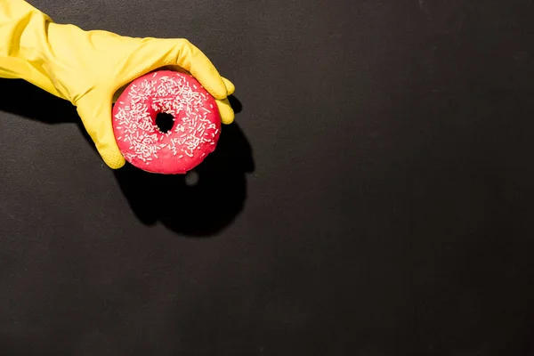 Teilansicht einer Frau in Gummihandschuhen mit Donut auf dunklem Hintergrund — Stockfoto