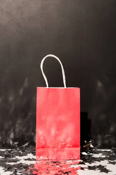 Red shopping bag standing on sparkle confetti on black background — Stock Photo
