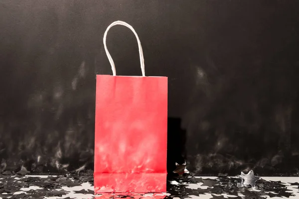 Red shopping bag standing on confetti on dark background — Stock Photo