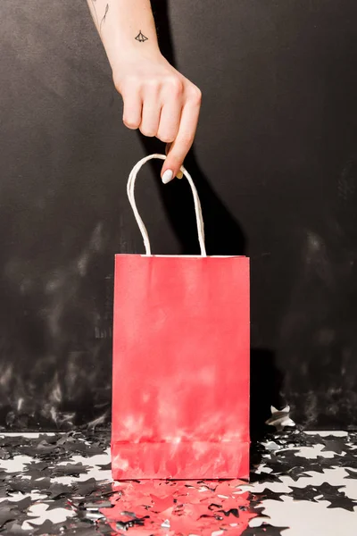 Partial view of girl with tattooes holding pink shopping bag on black background — Stock Photo