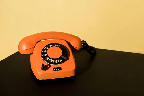 Vieux téléphone orange debout sur la surface noire sur fond jaune — Photo de stock