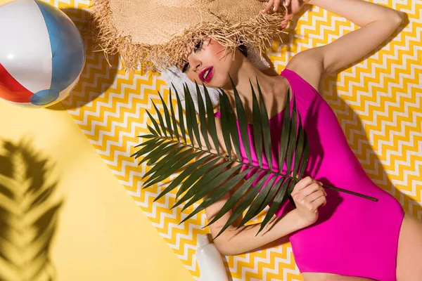 Vue du dessus de la charmante femme en maillot de bain rose tenant la plante verte et couchée sur une serviette jaune — Photo de stock
