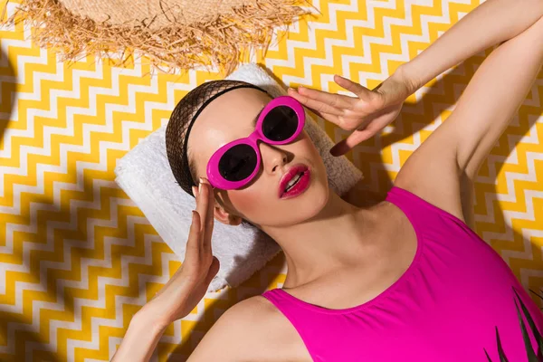 Woman in sunglasses and swimsuit lying on towel on yellow background — Stock Photo