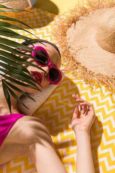 Розслаблена молода жінка в сонцезахисних окулярах лежить на жовтому рушнику — Stock Photo