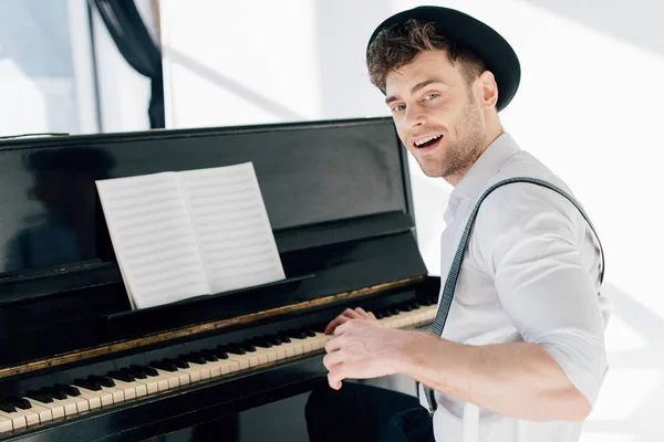 Pianista sonriente sentado junto al piano y mirando a la cámara - foto de stock