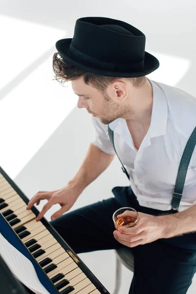 Pianiste élégant tenant un verre de boisson alcoolisée tout en jouant du piano — Photo de stock