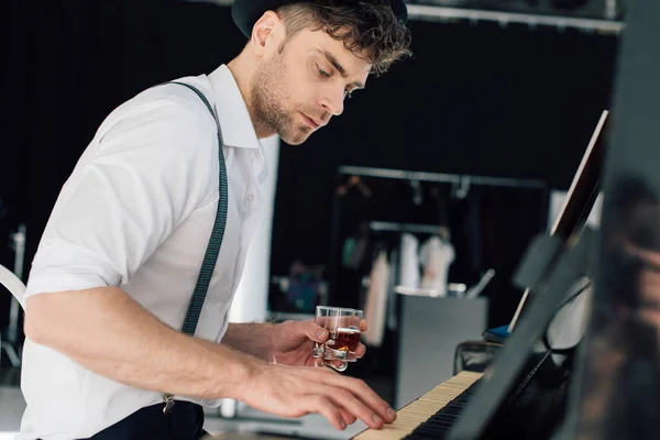 Selektiver Fokus des gut aussehenden Pianisten, der Klavier spielt und ein Glas Alkohol in der Hand hält — Stockfoto