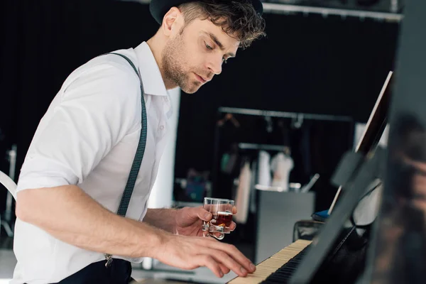 Messa a fuoco selettiva del pianista bello che suona il pianoforte e che tiene il vetro della bevanda dell'alcool — Foto stock