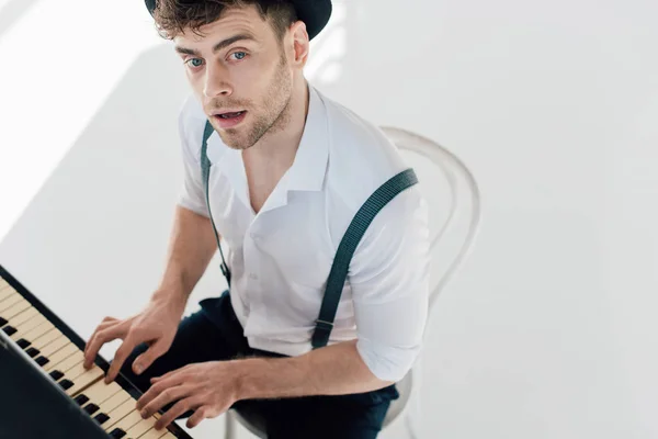 Guapo pianista en camisa blanca y sombrero negro tocando el piano - foto de stock