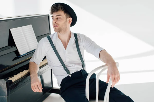 Beau musicien songeur assis sur une chaise blanche et appuyé sur le piano — Photo de stock