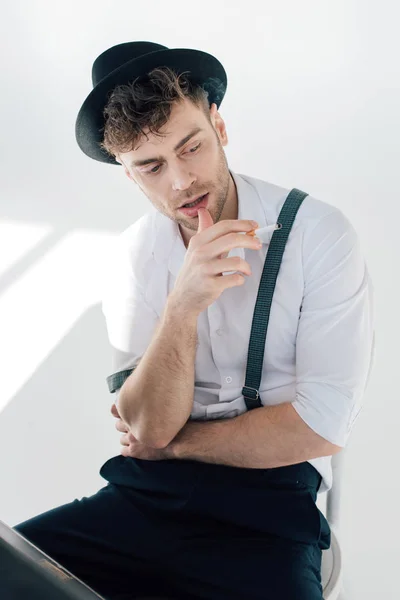 Красивий чоловік у білій сорочці і чорний капелюх тримає сигарету — стокове фото