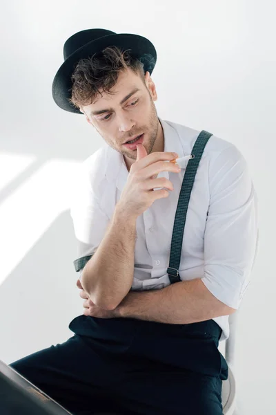 Homem bonito em camisa branca e chapéu preto segurando cigarro — Fotografia de Stock