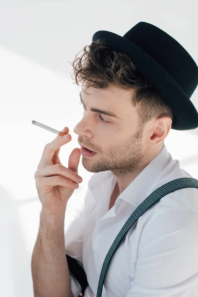 Bel homme en chemise blanche et chapeau noir fumant cigarette — Photo de stock