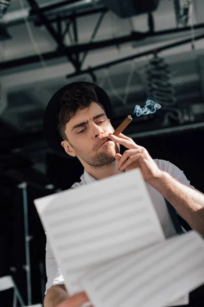 Selective focus of handsome musician holding music book sheets and smoking cigar — Stock Photo