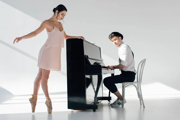 Guapo pianista jugando mientras hermosa bailarina bailando cerca de piano - foto de stock