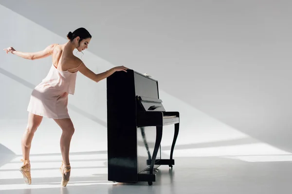 Beautiful young ballerina dancing in sunlight near black piano — Stock Photo