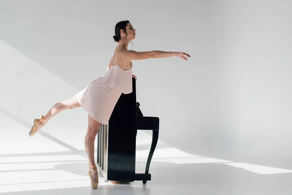 Jeune belle ballerine dansant près de piano noir — Photo de stock
