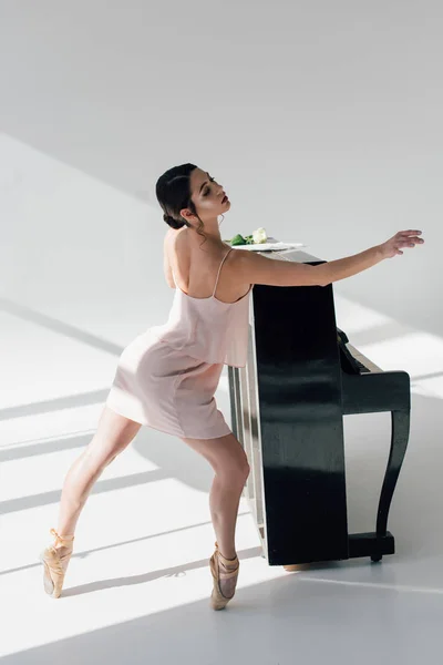 Молодая привлекательная балерина танцует рядом с черным фортепиано — стоковое фото