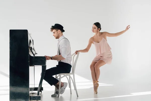 Красивый музыкант играет на пианино в то время как красивая балерина танцует возле стула — стоковое фото