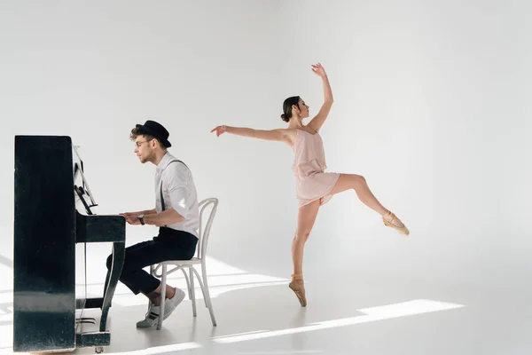 Красивый пианист играет на пианино, пока молодая балерина танцует в розовом платье — стоковое фото
