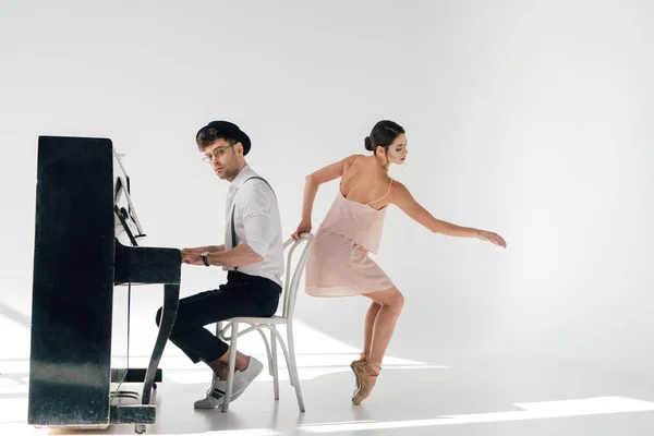 Красивый пианист играет на пианино в то время как изящная балерина танцует рядом с его стулом — стоковое фото