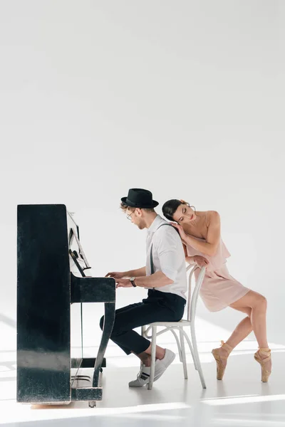 Bella giovane ballerina appoggiata al pianista seduta al pianoforte — Foto stock