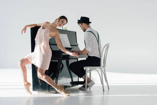 Joven músico tocando el piano mientras elegante bailarina bailando cerca de él - foto de stock