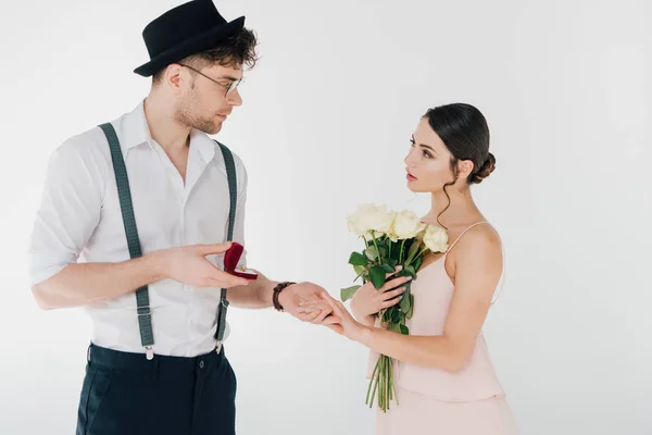 Hombre guapo en ropa de moda haciendo propuesta de matrimonio a hermosa chica sosteniendo ramo de rosas - foto de stock