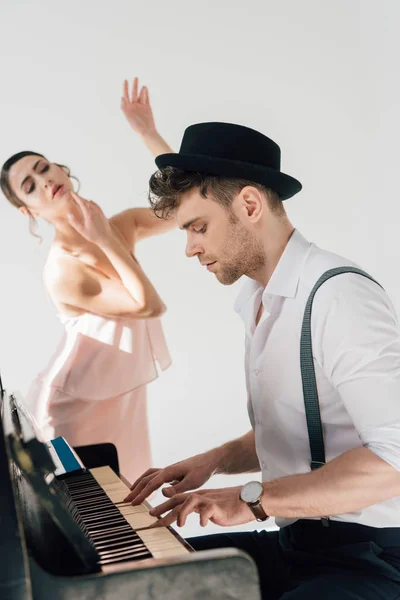 Enfoque selectivo de pianista guapo tocando el piano mientras la joven bailarina baila cerca de él - foto de stock
