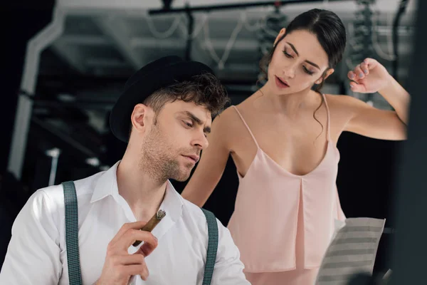 Beautiful ballerina standing near serious composer looking at music book and holding cigar — Stock Photo