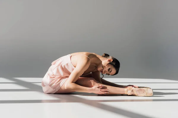 Young ballerina in pink dress sitting and stretching on floor — Stock Photo