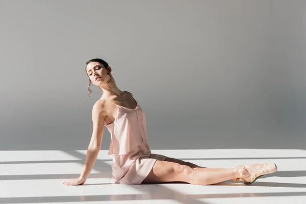 Giovane ballerina in abito rosa seduta sul pavimento alla luce del sole — Foto stock