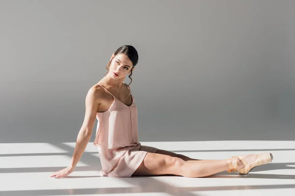 Jolie ballerine en robe rose assise sur le sol à la lumière du soleil — Photo de stock